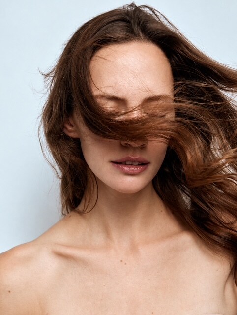 Portrait mit offenem, bewegtem Haar vor hellblauem Studiohintergrund
